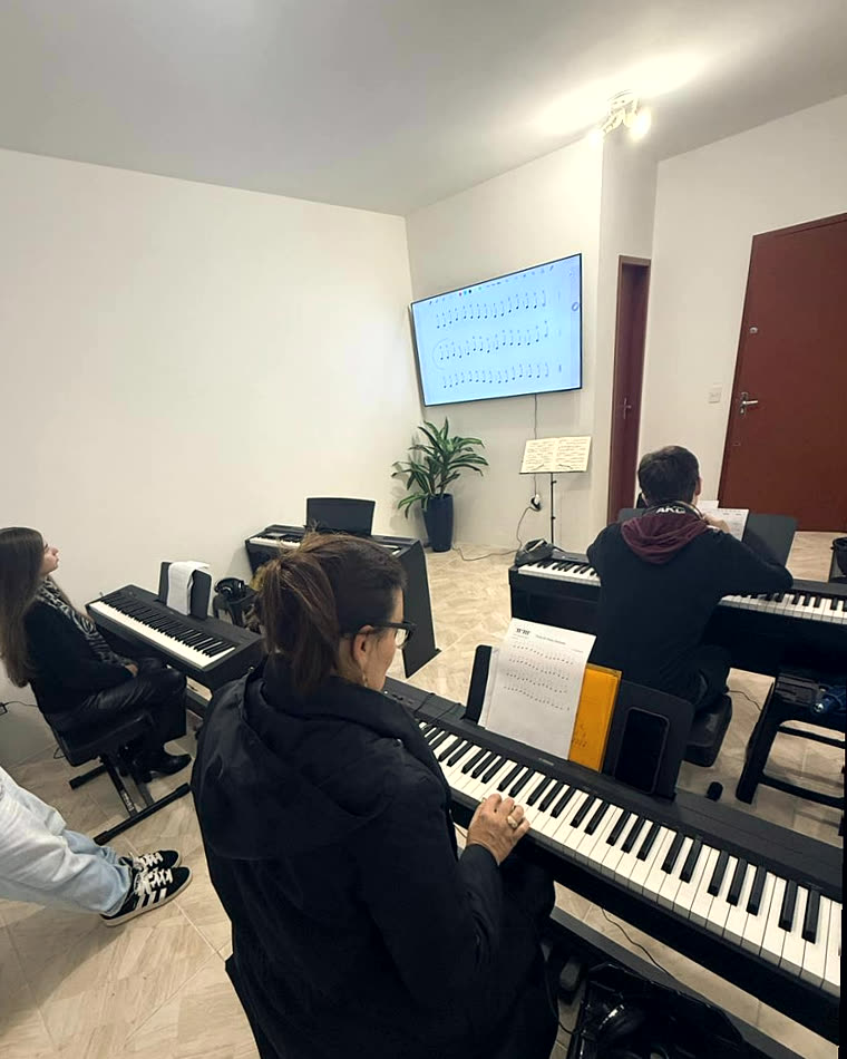 Alunos estudando em pianos digitais do Studio88, com fones e partitura na tela