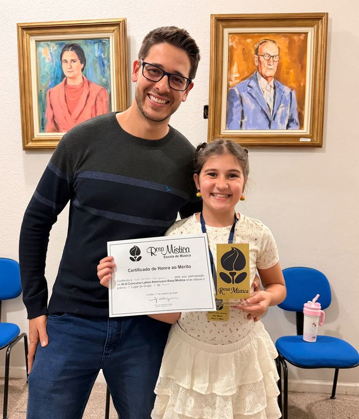 Nicole com o certificado de primeiro lugar e o troféu do XLIII Concurso Latino Americano Rosa Mística, ao lado do professor Arílton, em Curitiba